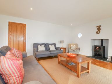 A living room with two gray sofas a wooden coffee table a small armchair a wood burning stove and a wooden door at Freefolk in Polzeath