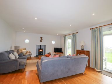 A living room with gray sofas a wood stove and a television at Freefolk in Polzeath