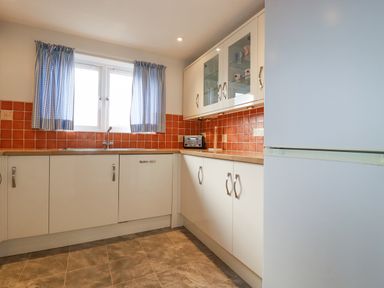 A kitchen with white cabinets orange tiled backsplash a window with blue checked curtains and a white refrigerator at Freefolk in Polzeath