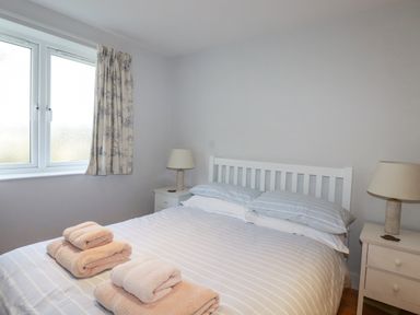 A bedroom with a double bed folded towels bedside tables with lamps and a window with curtains at Freefolk in Polzeath