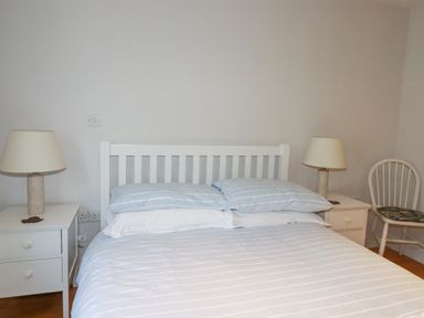 A bedroom with a white bed frame two bedside tables with lamps and a white chair at Freefolk in Polzeath
