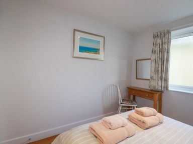 A bedroom with a bed having folded towels on it a wooden desk a chair and a window with curtains at Freefolk in Polzeath