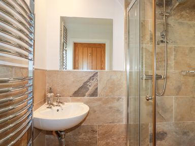 A bathroom with a small sink, mirror, heated towel rail, and a glass shower enclosure with tiled walls at Freefolk in Polzeath