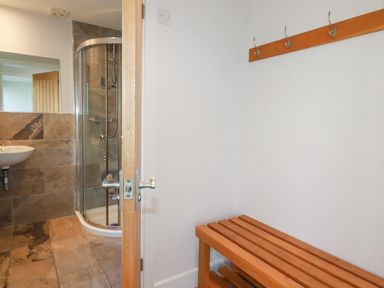 A room with wooden bench and hooks on the wall next to a bathroom with a shower and sink at Freefolk in Polzeath
