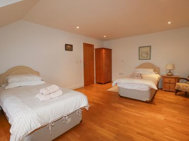 A bedroom with two single beds a wooden wardrobe a nightstand with lamp and an armchair at Freefolk in Polzeath
