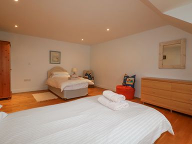 A bedroom with two beds a wooden wardrobe a dresser with a mirror and a chair with cushions at Freefolk in Polzeath