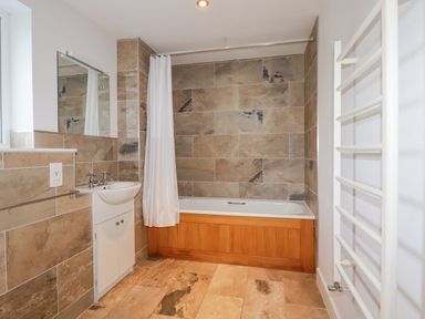A bathroom with a bathtub, white shower curtain, sink with cabinet, wall mirror, and heated towel rail at Freefolk in Polzeath
