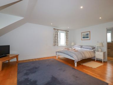 A bedroom with a bed two bedside tables lamps a window with curtains a rug and a television on a wooden table at Freefolk in Polzeath
