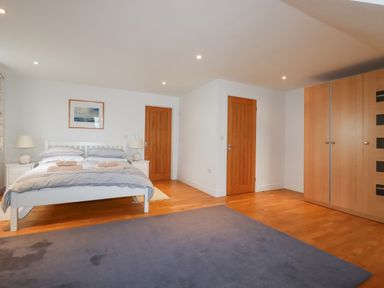 A bedroom with a double bed bedside tables lamps wooden doors a large wardrobe and a rug on the floor at Freefolk in Polzeath