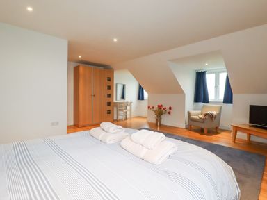 A bedroom with a bed and folded towels a wooden wardrobe a dressing table an armchair a TV and a vase with flowers at Freefolk in Polzeath