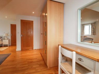 A bedroom with wooden floor wooden wardrobe white desk chair and mirror at Freefolk in Polzeath