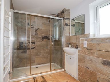 A bathroom with a glass shower enclosure a white sink with cabinet and a window at Freefolk in Polzeath