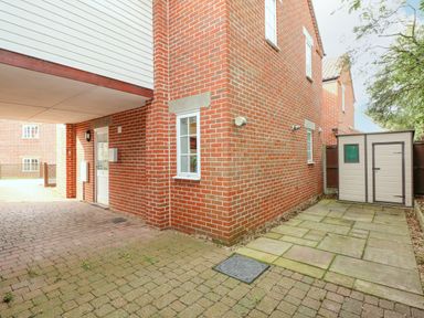 An exterior view of a brick building with a paved driveway and a plastic storage shed at The Mill Stones in Stalham