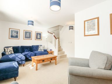 A living room with blue sofas wooden coffee table framed pictures and stairs at The Mill Stones in Stalham
