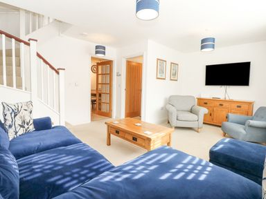 A living room with blue and gray chairs a wooden coffee table a wooden sideboard and a wall-mounted television at The Mill Stones in Stalham