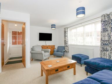 A living room with armchairs a wooden coffee table a sideboard and a wall-mounted television at The Mill Stones in Stalham