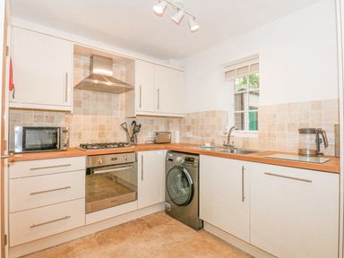 A kitchen with white cabinets wooden countertops a washing machine a microwave oven a toaster a kettle and a window at The Mill Stones in Stalham