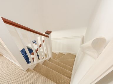 A carpeted staircase with white railings and wooden handrail at The Mill Stones in Stalham