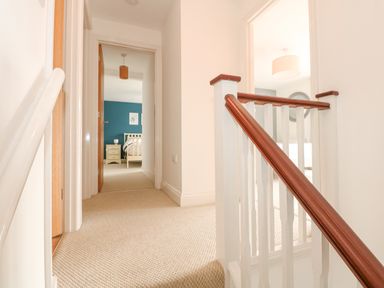 A carpeted hallway with white walls and wooden handrails leading to bedrooms at The Mill Stones in Stalham