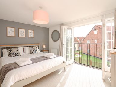 A bedroom with a bed cushions bedside tables and an open balcony door at The Mill Stones in Stalham