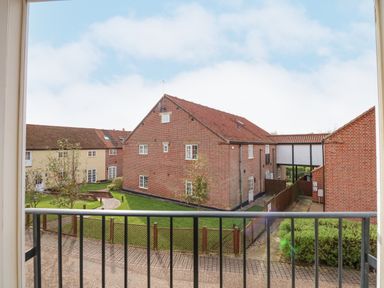 A view of brick and yellow buildings with a grassy courtyard and a pathway seen from a balcony at The Mill Stones in Stalham
