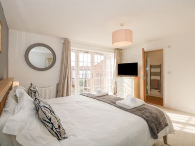 A bedroom with a bed pillows a chest of drawers with a television and a door leading to a bathroom at The Mill Stones in Stalham