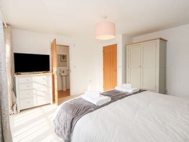 A bedroom with a bed folded towels a chest of drawers with a television and a wardrobe at The Mill Stones in Stalham