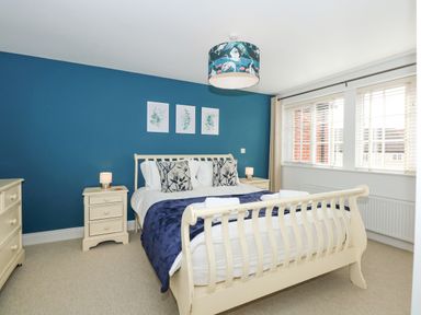 A bedroom with a cream bed frame blue wall two bedside tables and a dresser at The Mill Stones in Stalham