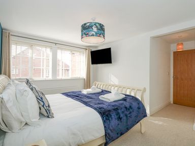 A bedroom with a bed folded towels a window with blinds a wall mounted tv and a wooden door at The Mill Stones in Stalham