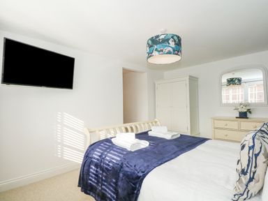 A bedroom with a bed covered with a blue throw and two folded towels a wardrobe a dresser with a mirror and a wall-mounted television at The Mill Stones in Stalham