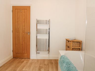 A bathroom with a wooden door a metal towel rack a wicker drawer unit and a bathtub with a blue towel at The Mill Stones in Stalham