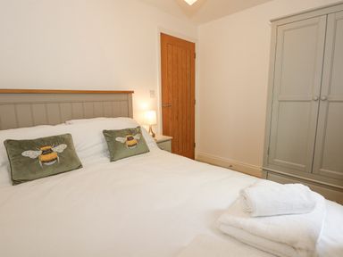 A bedroom with a bed featuring bee cushions a wooden door a lamp on a bedside table and a wardrobe at The Mill Stones in Stalham