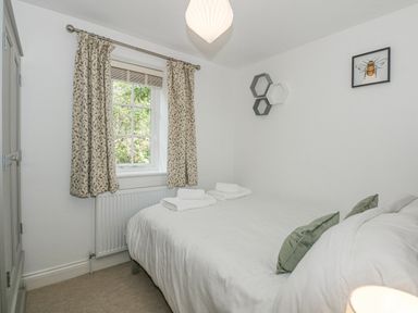 A bedroom with a bed between a window with patterned curtains and a wall with hexagonal shelves and a bee picture at The Mill Stones in Stalham