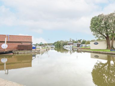 A river with boats docked along the banks and buildings on each side at The Mill Stones in Stalham