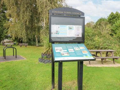 A public notice board in a grassy area with benches and trees at The Mill Stones in Stalham