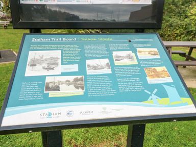 An outdoor information board about Stalham Staithes on a stand with park benches and grass in the background at The Mill Stones in Stalham
