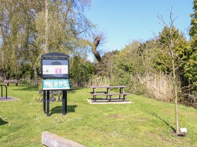 A picnic bench and a signboard on a grassy area with trees at The Mill Stones in Stalham