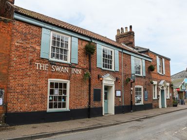 A brick building with blue shutters and two entrances labeled The Swan Inn on a street