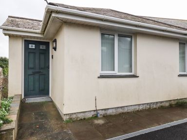 A front entrance with a dark green door and two adjacent windows in a single-story building at Freefolk Cottage in Polzeath