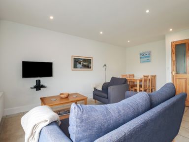 A living room with blue couches a wooden coffee table a wall-mounted television and a dining table with chairs at Freefolk Cottage in Polzeath