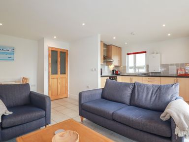 An open living room and kitchen with blue sofas a wooden door and light wood kitchen cabinets at Freefolk Cottage in Polzeath