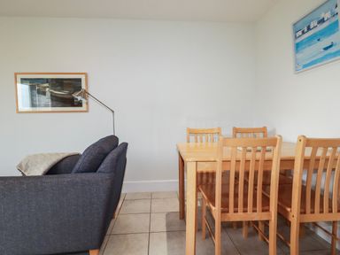 A living room with a gray sofa and a wooden dining table with six chairs at Freefolk Cottage in Polzeath