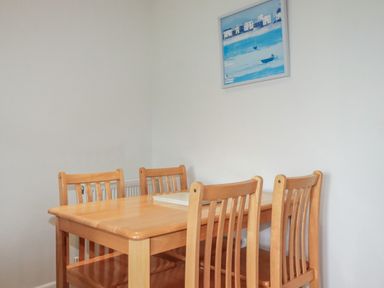 A wooden dining table with four chairs and a blue painting on a white wall at Freefolk Cottage in Polzeath