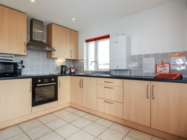 A kitchen with wooden cabinets a black countertop a built in oven microwave kettle toaster and a window at Freefolk Cottage in Polzeath