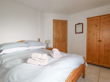 A bedroom with a wooden bed with light blue bedding towels on the bed a wooden wardrobe a wooden door and a small bedside table with a lamp at Freefolk Cottage in Polzeath