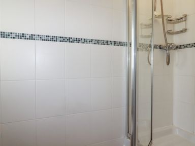 A shower area with white tiled walls and a glass shower door at Freefolk Cottage in Polzeath