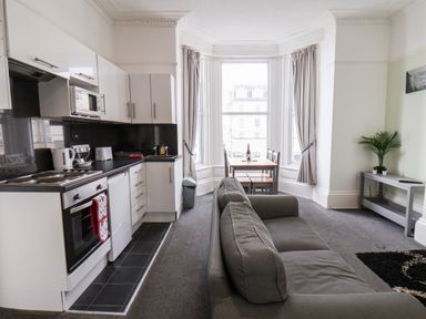 A kitchen and living area with white cabinets gray sofa dining table and large windows at Promenade in Bridlington