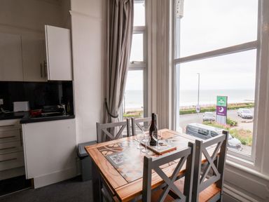 A dining table with four chairs near large windows overlooking a street and the sea at Promenade in Bridlington