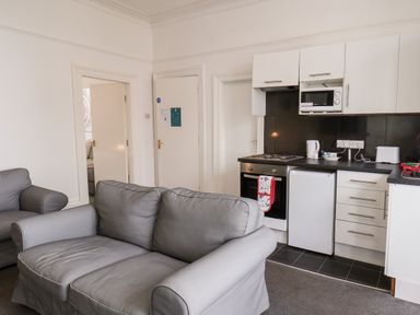 A living room with grey sofas and a compact kitchen area with appliances at Promenade in Bridlington