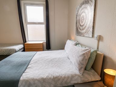 A bedroom with two beds a bedside table with a lamp a chest of drawers and a window at Promenade in Bridlington